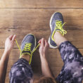 Closeup of person tying their running shoes while sitting on a wood floor