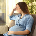 Pregnant person holding head and frowning