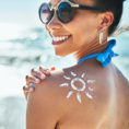 Person wearing sunglasses at the beach with sunscreen in the shape of the sun on their shoulder