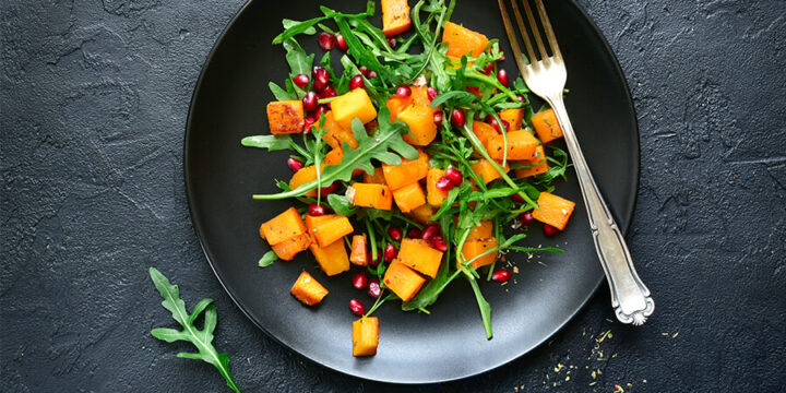 Salad topped with roasted squash and pomegranates
