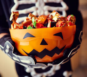 Child in costume holding jack-o'-lantern bucket full of Halloween candy