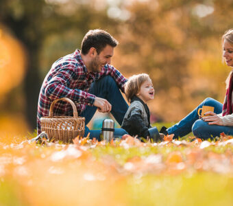 Parents and child sitting on blanket outdoors during fall season