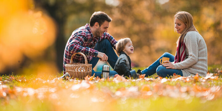 Parents and child sitting on blanket outdoors during fall season