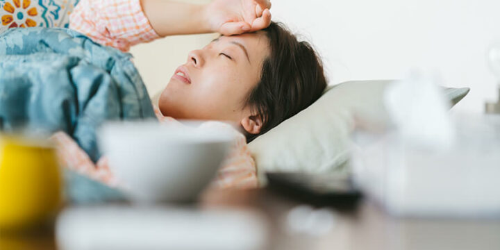 Sick person lying in bed with hand to forehead