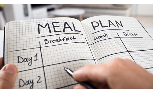 Person writing in meal plan food diary