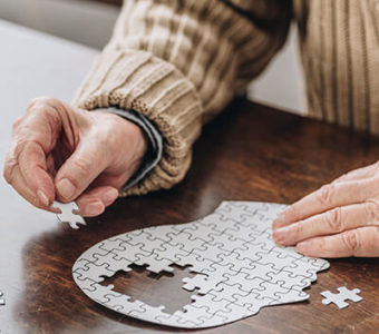 Person putting together puzzle pieces in the shape of a human head, pieces missing from brain area