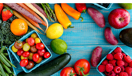 Rainbow collection of fruits and vegetables sitting on blue wood table