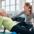 Older adult using foam roller with help from a physical therapist