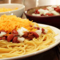 Plate of spaghetti with chili, onions and shredded cheese on top