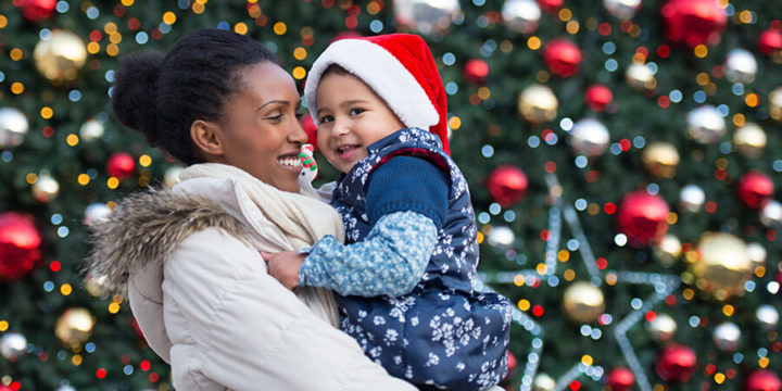Smiling woman holding child standing in front of holiday decorations