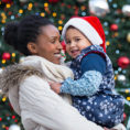Smiling woman holding child standing in front of holiday decorations
