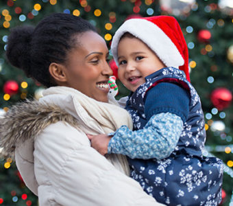 Smiling woman holding child standing in front of holiday decorations