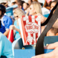 Person holding a container of popcorn in a sports stadium