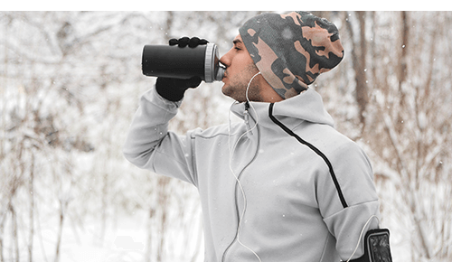Man drinking from water bottle wearing winter exercise gear outside