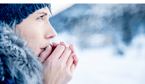Woman outside during the winter blowing on her hands and creating air condensation