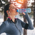 Woman drinking from water bottle while exercising outside during the winter