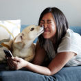 Woman laying on a couch with a dog licking her face