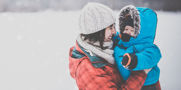 Woman holding baby, both in winter clothing, standing outside in the snow