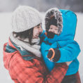 Woman holding baby, both in winter clothing, standing outside in the snow