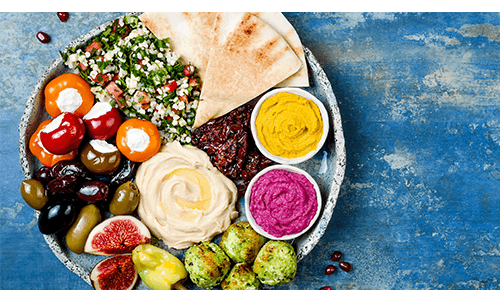 Plate full of a variety of mediterranean food including vegetables and hummus