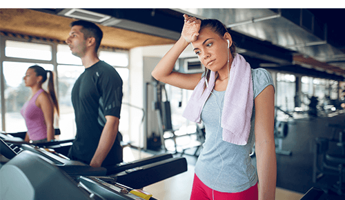 Woman wiping forehead after working out on a treadmill in a gym