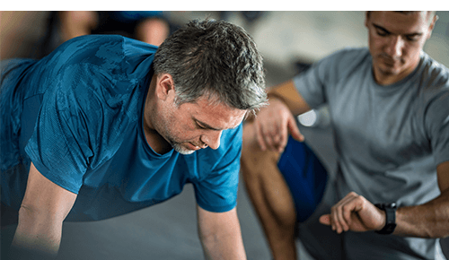 Man performing plank during exercise supervised by fitness professional