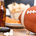 Football in front of bowls of snack foods and drink bottles on table