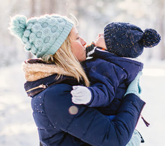 Mother holding baby, both wearing cold weather gear, in winter outside