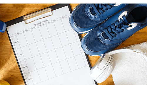Exercise shoes, headphones and a clipboard with a blank workout plan on it Exercise shoes, headphones and a clipboard with a blank workout plan on it