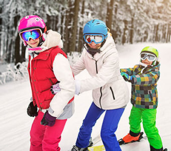 Three children holding on to each while skiing down a snow covered mountain