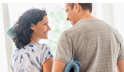 Couple smiling at each other while holding yoga mats