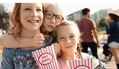 Three smiling siblings standing outside and holding containers of popcorn