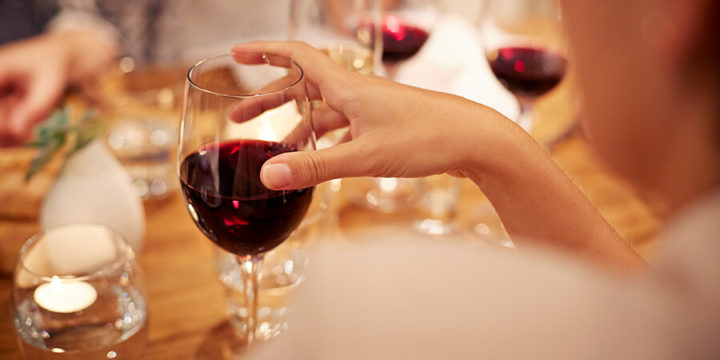 Closeup of a group of people holding wine glasses full of red wine around a dinner table