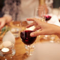 Closeup of a group of people holding wine glasses full of red wine around a dinner table