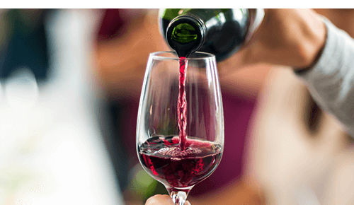 Person pouring red wine from a bottle into a wine glass