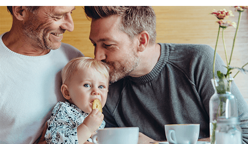 Parents and young child eating food at a table with coffee cups on it Parents and young child eating food at a table with coffee cups on it