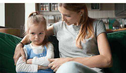 Woman talking to an upset looking child while sitting on a couch Woman talking to an upset looking child while sitting on a couch
