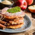 Stack of apple pancakes on a plate with cinnamon sticks and powdered sugar