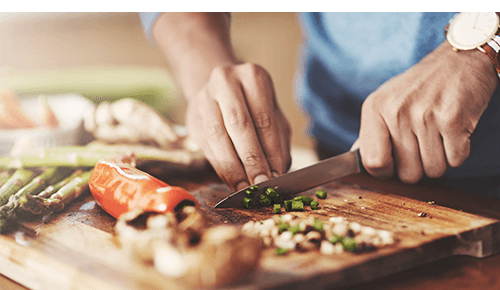 Closeup of person chopping vegetables with knife on cutting board