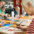 Group of older adults painting while seated at a table