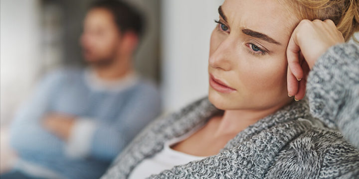A sad woman sitting with a man sitting behind her out of focus