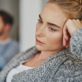 A sad woman sitting with a man sitting behind her out of focus