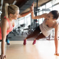 Two women high-fiving while working out, doing push-ups in a gym