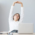 Person stretching their arms over their heads while seated at their desk in front of a computer