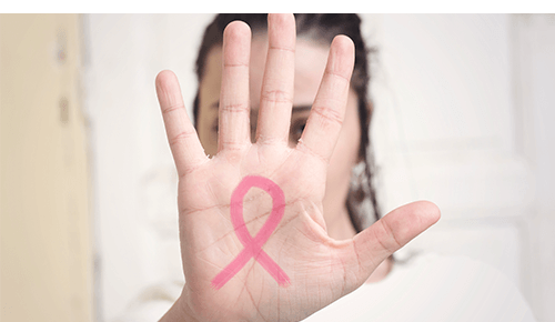 Person holding up their hand with a pink ribbon drawn on it to the camera