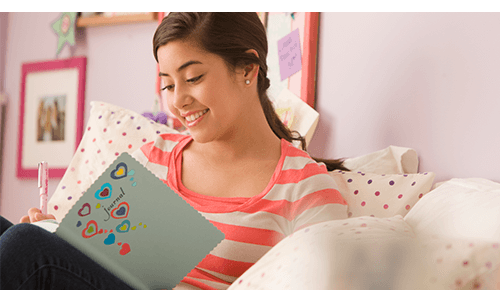 Teen writing in a journal while sitting in bed Teen writing in a journal while sitting in bed