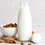 Glass bottle full of almond milk surrounded by raw almonds