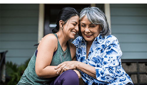 Adult daughter and mother smiling and hugging outdoor on porch Adult daughter and mother smiling and hugging outdoor on porch