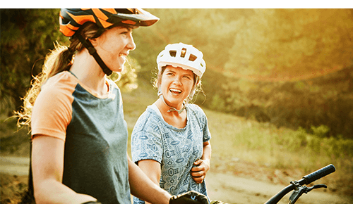 Two people with helmets on riding bicycles on an outdoor trail