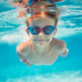 Young child wearing eye goggles swimming in a pool